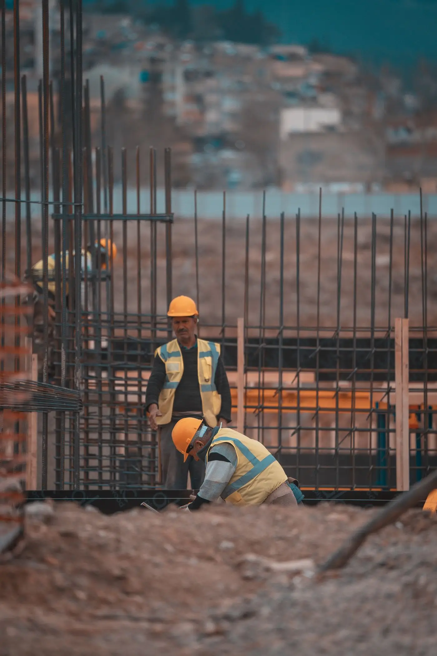 Steel fixers tying reinforcement bars in a column cage on a construction site at dusk.