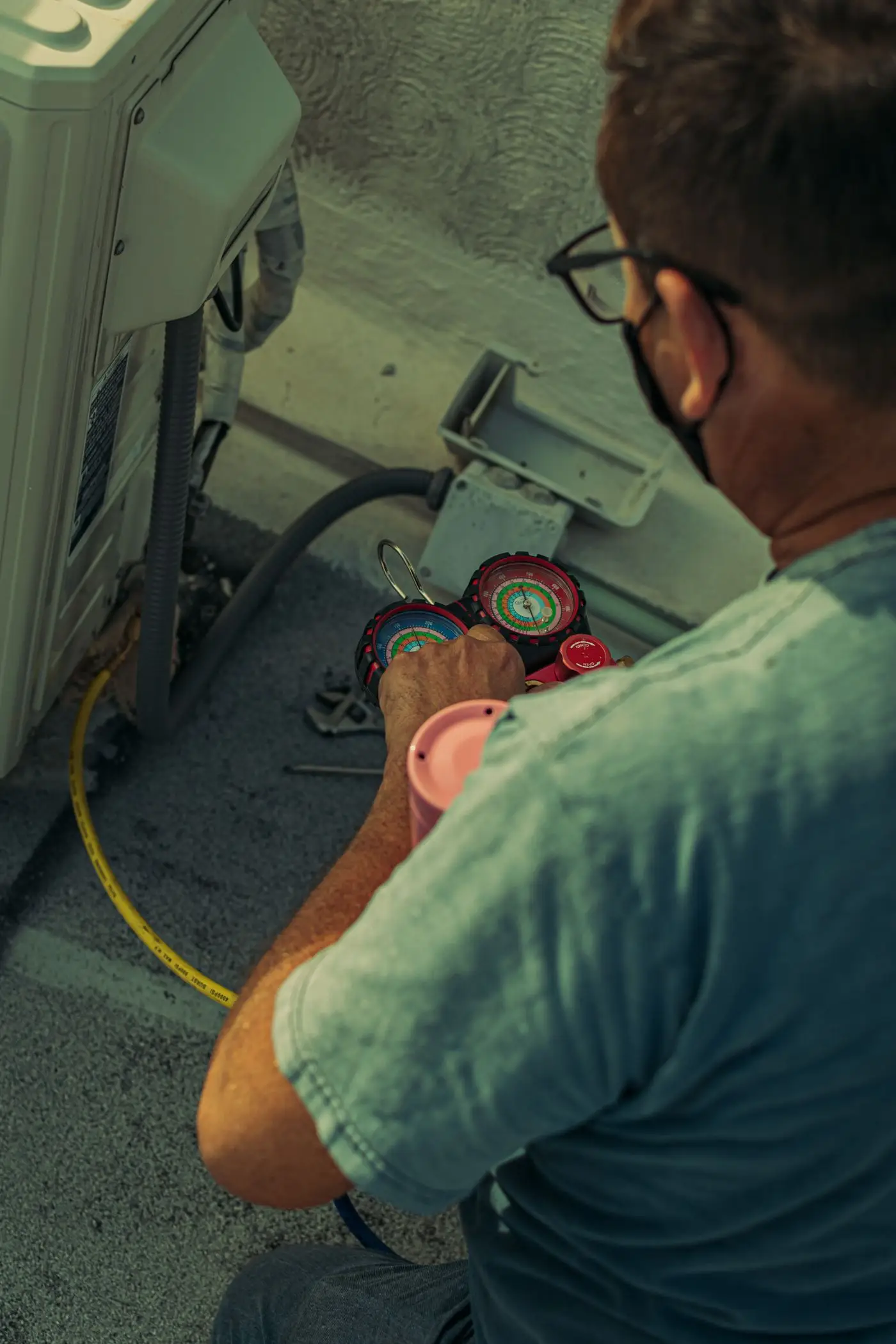 An HVAC technician connecting a refrigerant manifold gauge set to an outdoor condensing unit.